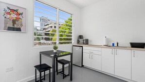 Una cocina moderna con armarios blancos, encimera negra, microondas, fregadero y ventana con vistas a edificios y follaje.