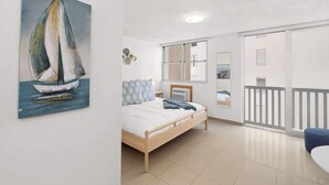 Een slaapkamer met een bed, een schilderij van een zeilboot, een raam en een balkon.