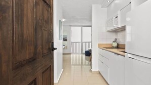 Een moderne keuken met witte kasten, een houten deur en uitzicht op een balkon.