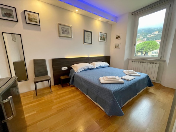 A bedroom with a bed, bedside table, chair, and a window with a view.
