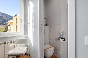 Un baño con inodoro, ducha y una silla junto a la ventana.