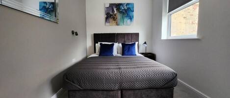 A bedroom with a bed, a window, and a painting on the wall.