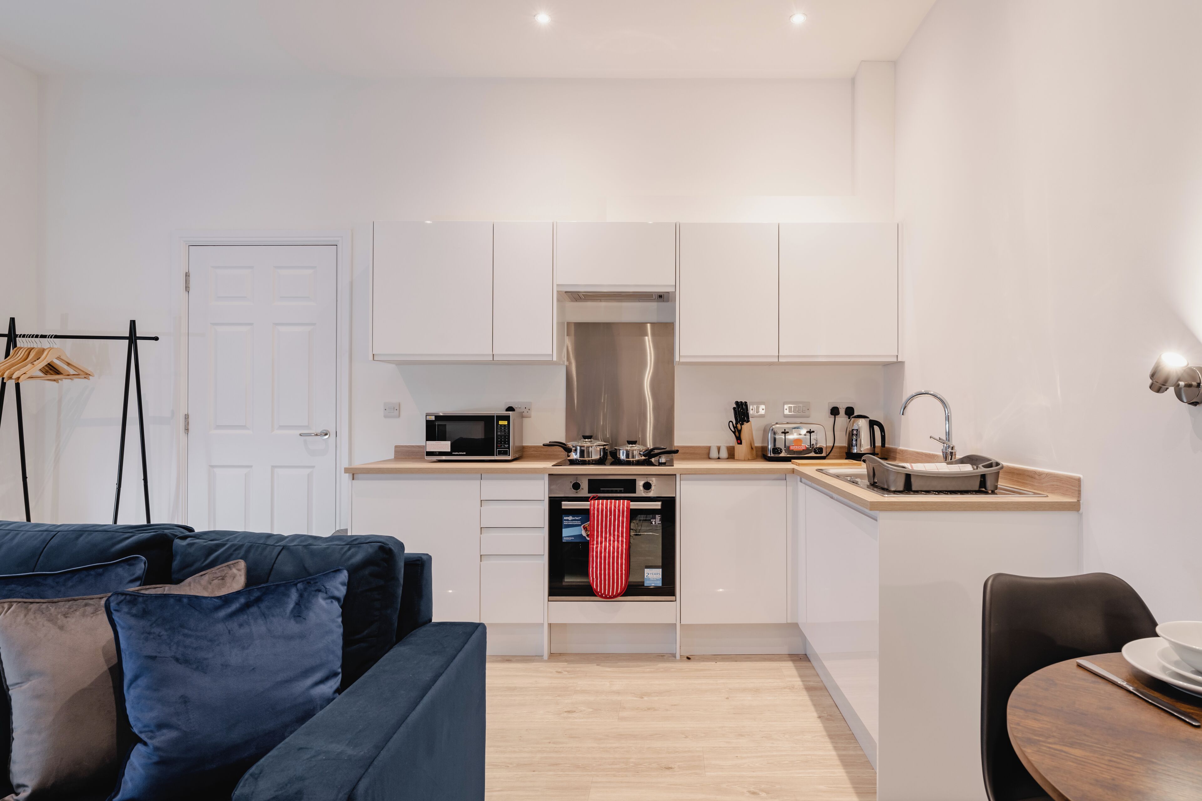 A modern kitchen with white cabinets, a microwave, a stove, and a sink. There is a wooden dining table with chairs.