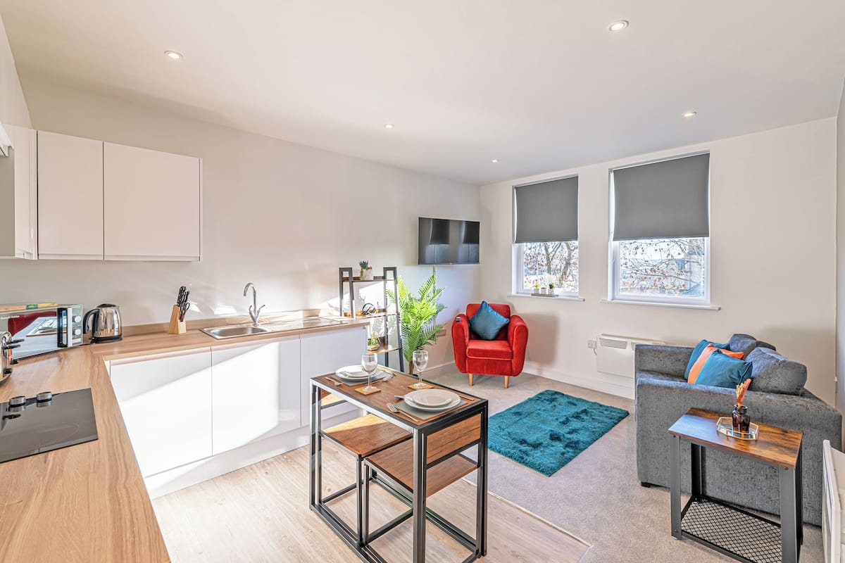 A modern kitchen with a dining area, a red chair, a grey sofa, and a blue rug.