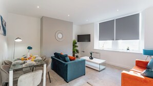 Uma sala de estar moderna com uma mesa de jantar de vidro, um sofá azul e uma poltrona laranja.