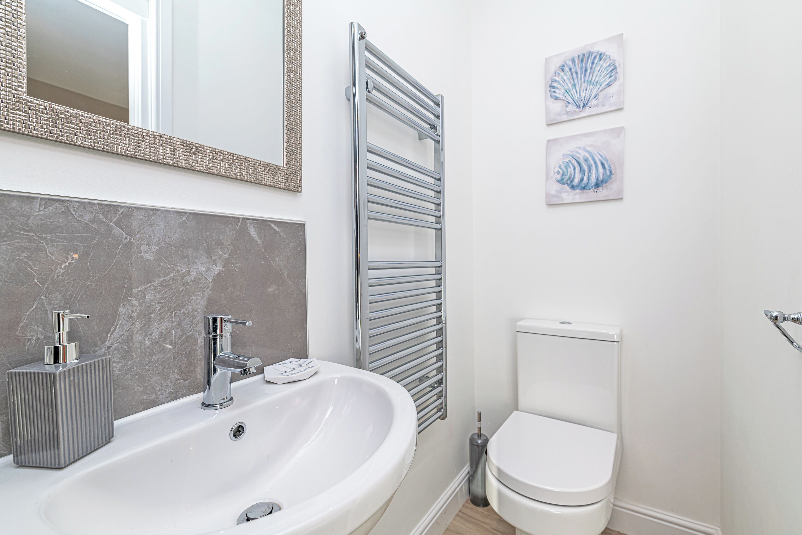 A modern bathroom with a large sink, chrome fixtures, a toilet, and two framed artworks on the wall.