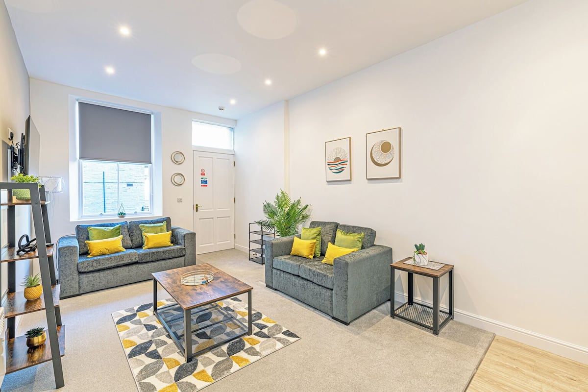 A modern living room with two grey sofas, a coffee table, and a small side table. There is a window with a view of the outside, and the room has a clean, minimalist design.