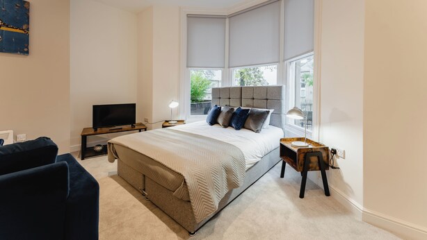 Quarto moderno com cama grande, televisão, escrivaninha e janela com persianas.