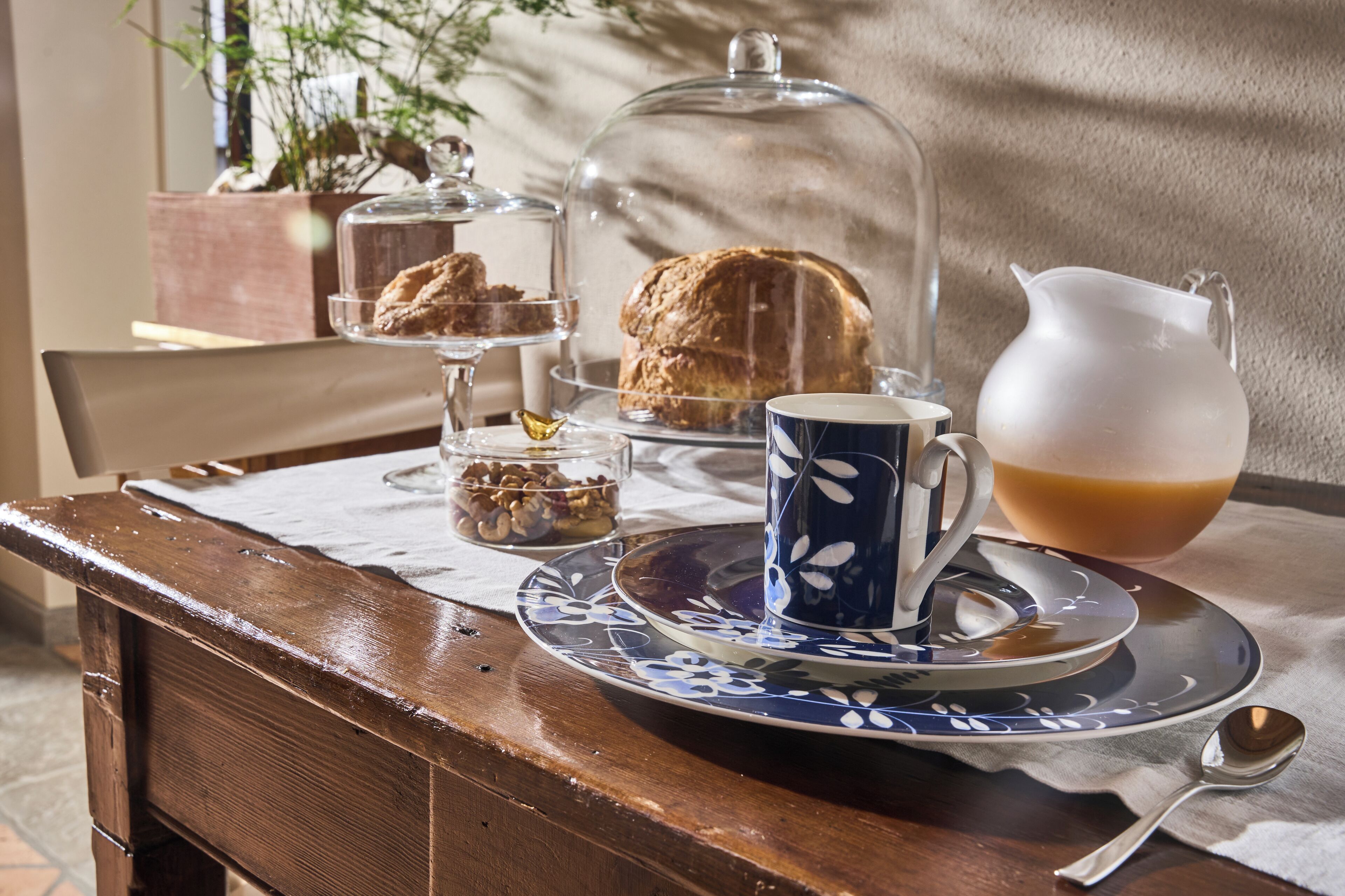 Uma mesa com prato, caneca, jarra e uma cúpula de vidro com doces.