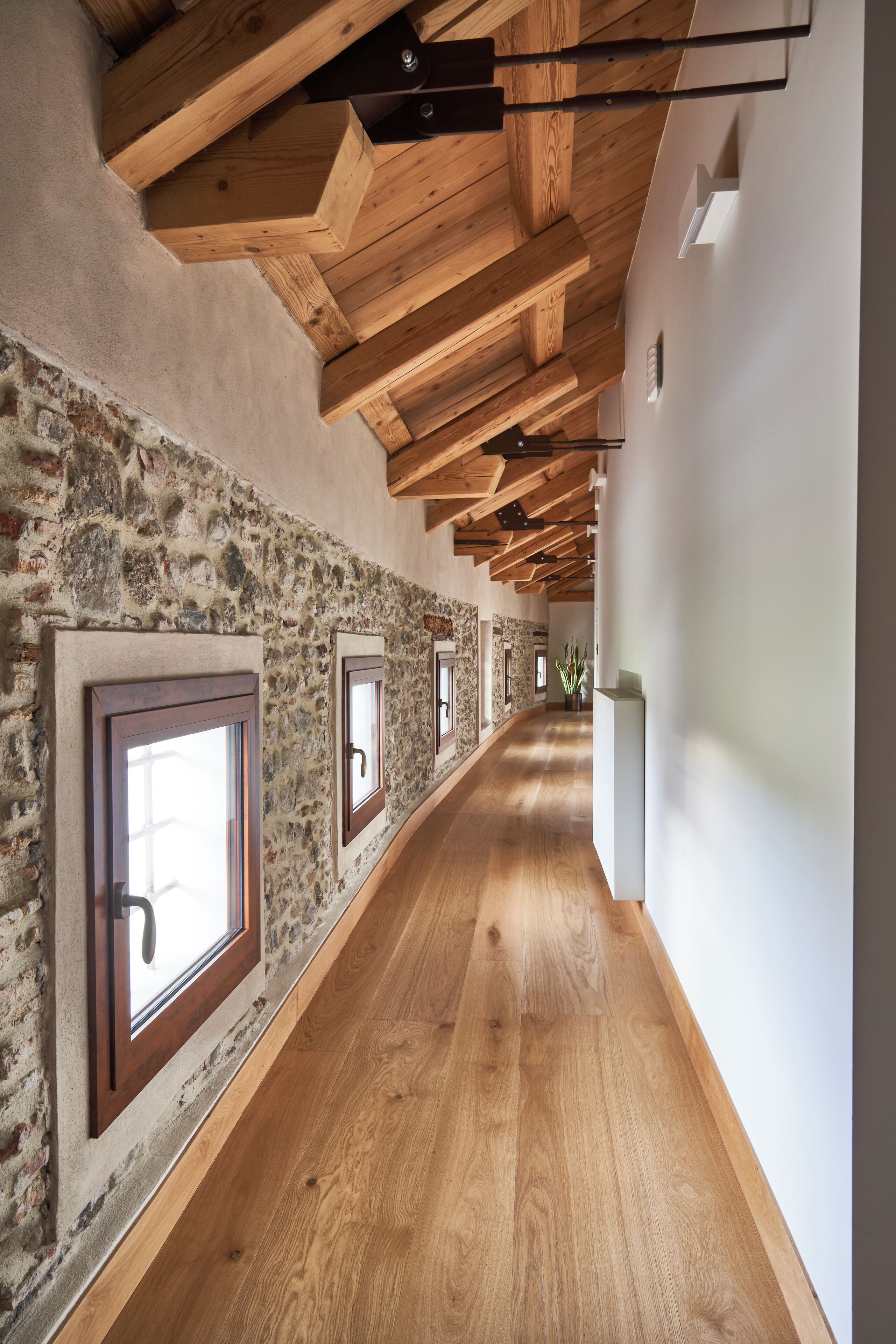 Un pasillo con vigas de madera a la vista, paredes de piedra y suelo de madera.