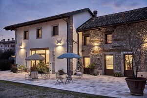 Un edificio de dos pisos con fachada de piedra y techo de tejas. Cuenta con un patio con mobiliario exterior y un paraguas grande.