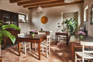 Un comedor rústico con una mesa y sillas de madera, rodeado de plantas en macetas y un amplio ventanal.