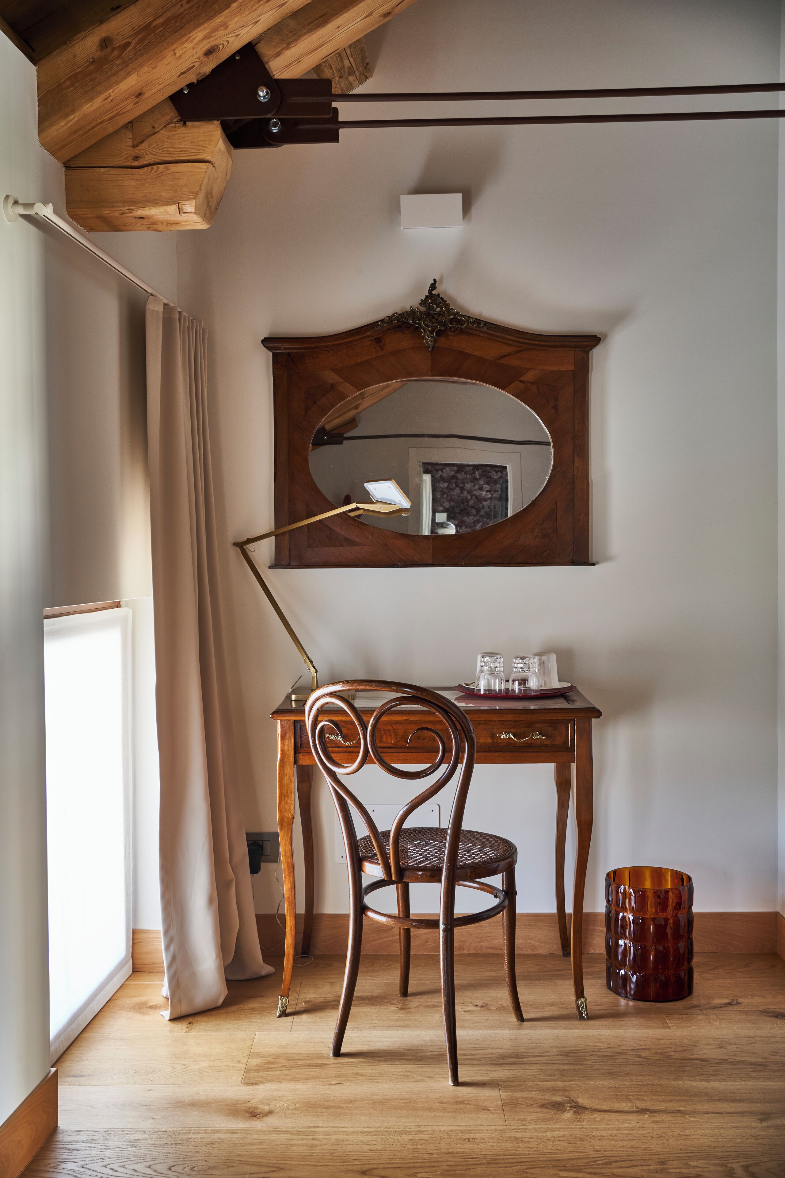 A room with a wooden desk, a chair, a mirror, and a small table with glasses.