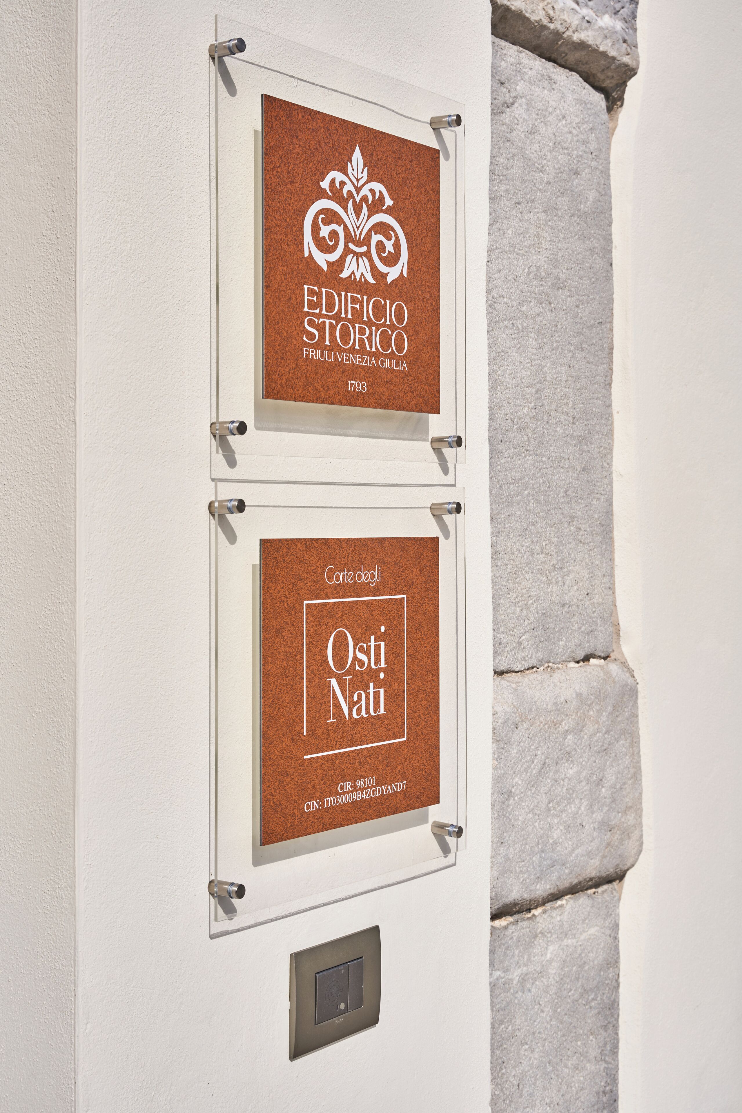 Zwei gerahmte Schilder an einer Wand, eines zeigt 'EDIFICIO STORICO' und das andere 'Corte degli Osti Nati'.
