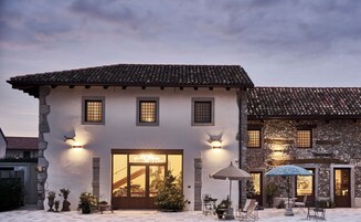 Un edificio tradicional con techo de tejas, puerta de madera y un pequeño patio con mobiliario exterior y sombrillas.