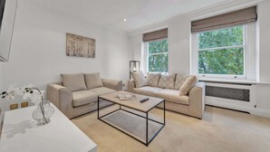 Ett modernt vardagsrum med två beige soffor, ett soffbord i glas och en tavla på väggen.