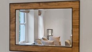 En spegel med en träram som speglar ett rum med ett fönster, en lampa och en soffa.