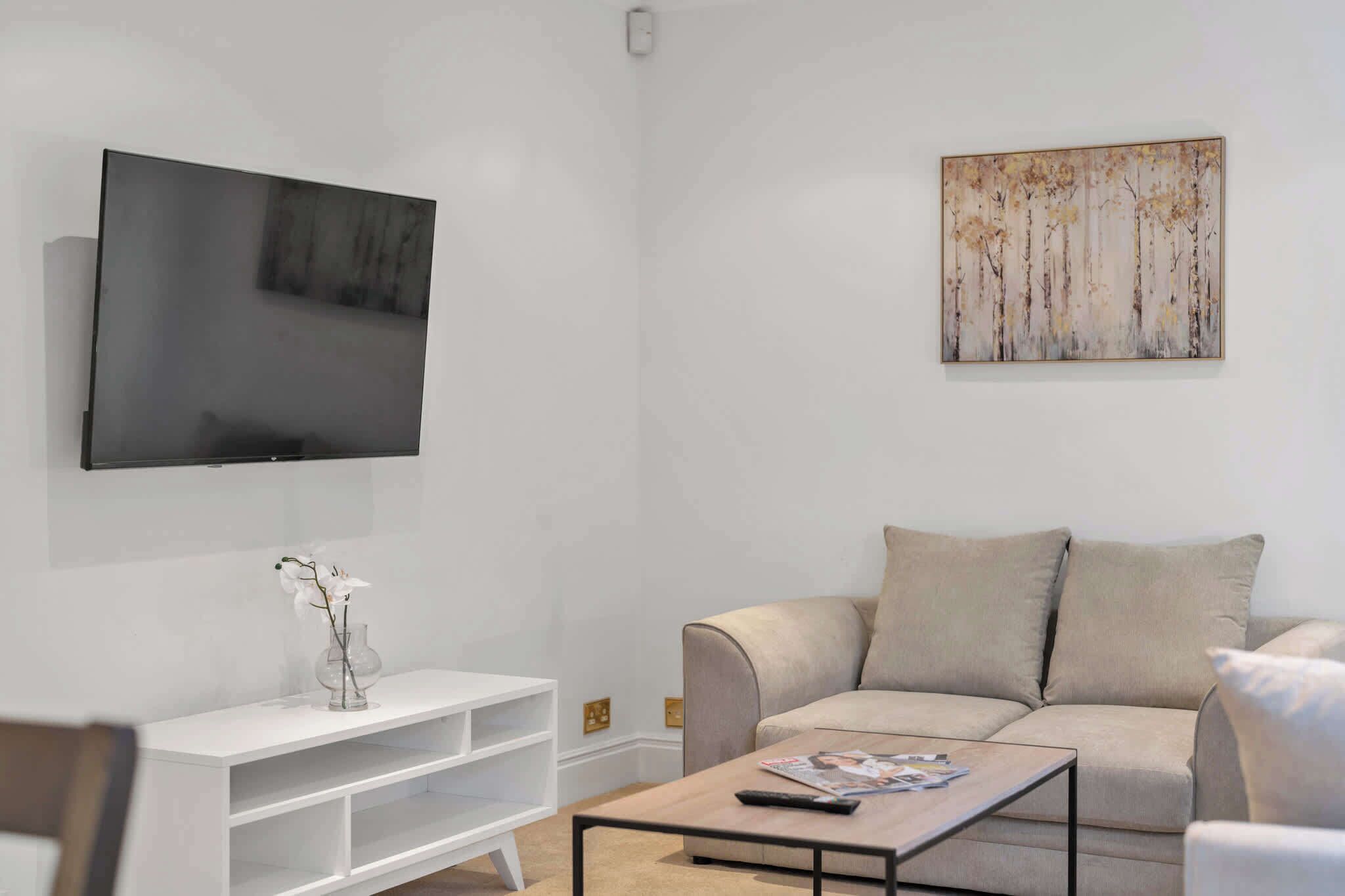 A modern living room with a flat-screen TV, a beige sofa, a coffee table, and a white entertainment unit.
