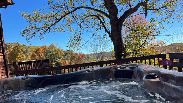 A hot tub with a wooden deck and a view of autumn trees in the background.