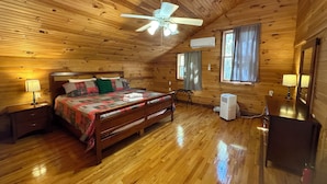 A cozy wooden cabin bedroom with a bed, nightstands, a ceiling fan, and a window with curtains.