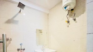 A bathroom with a toilet, sink, mirror, shower, and a small trash bin. - Roomshala Hotel Green Valley (New Delhi)