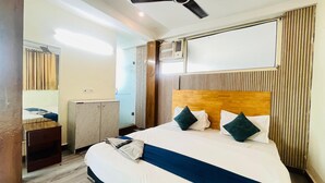 A hotel room with a bed, a ceiling fan, a radiator, a mirror, and a window with curtains. - Roomshala Hotel Green Valley (New Delhi)