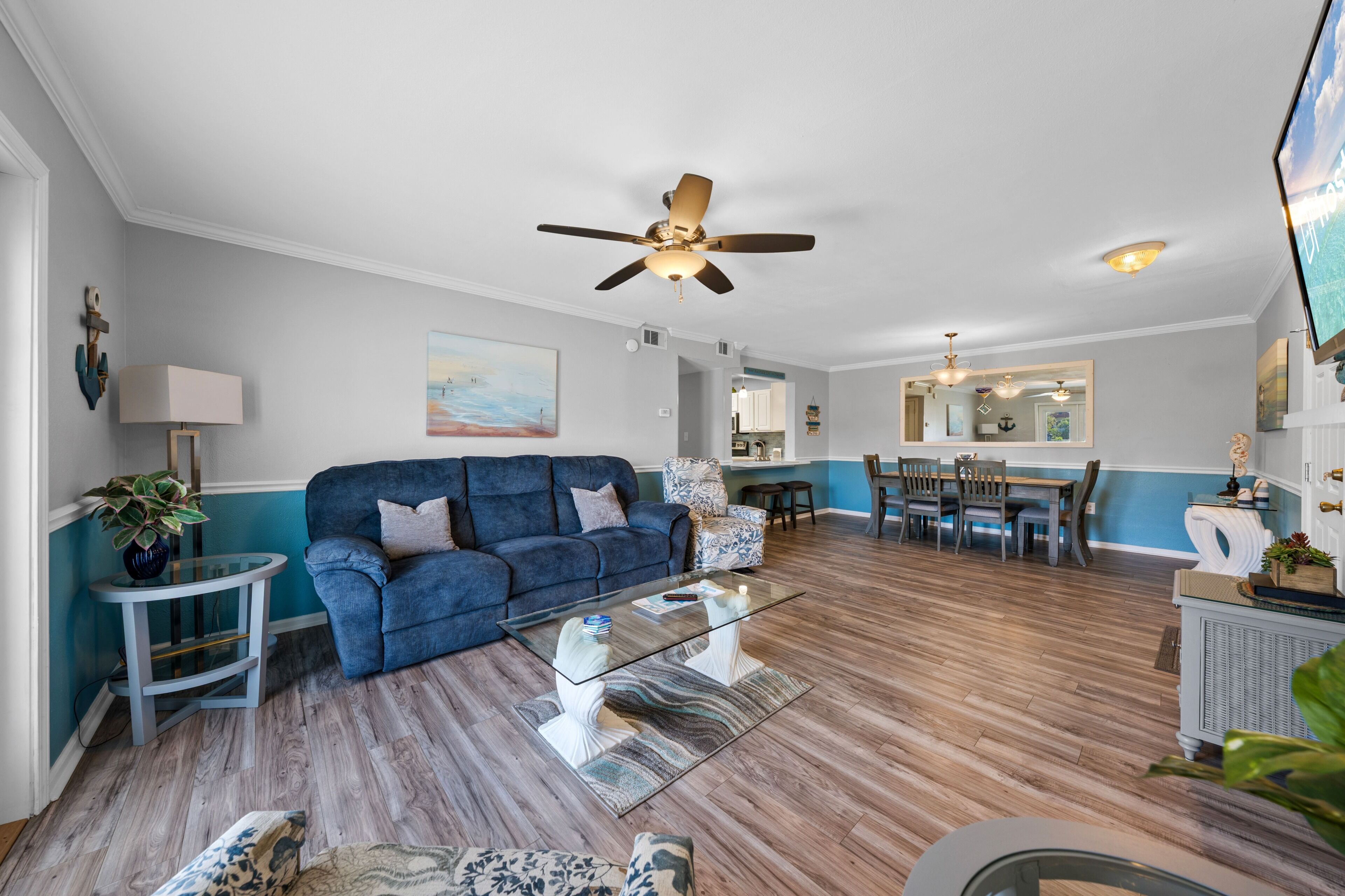 A living room with a blue sofa, glass coffee table, and a ceiling fan.