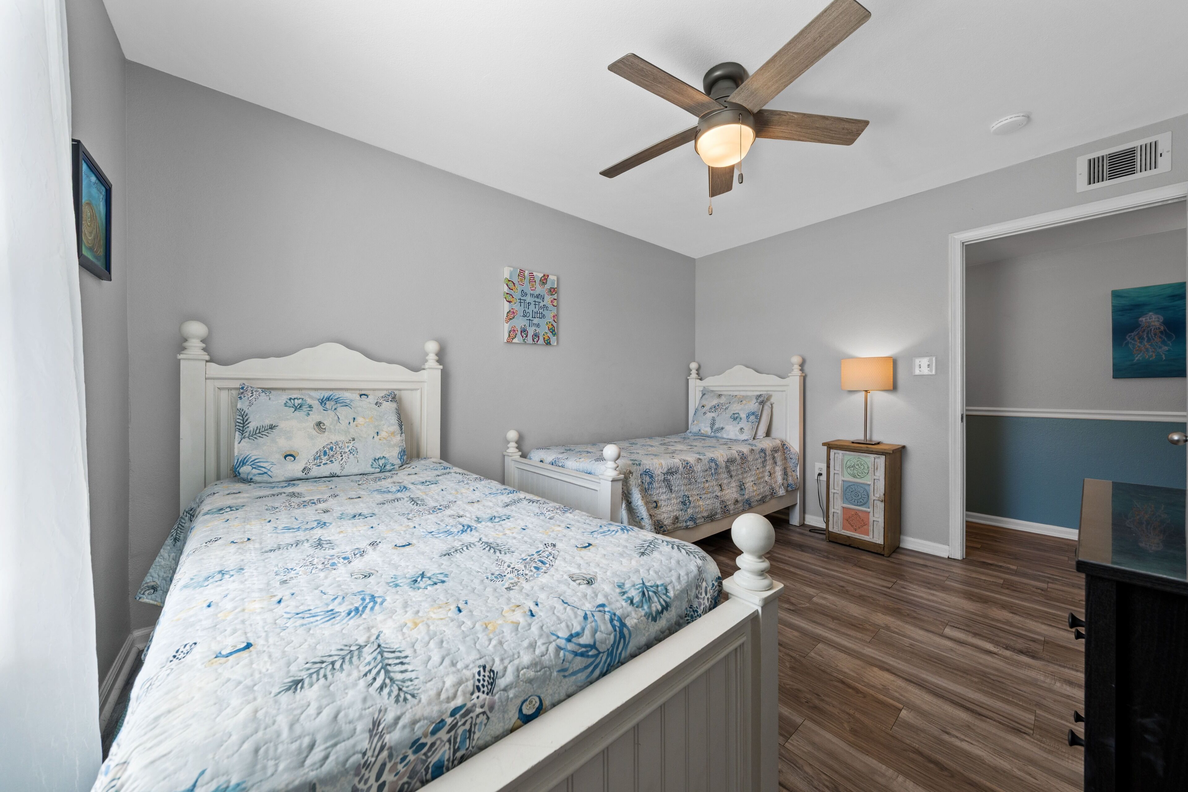 A bedroom with two beds, a ceiling fan, a nightstand, and a wall art piece.