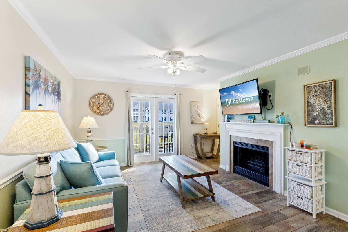 A living room with a sofa, a coffee table, a television, a fireplace, and a ceiling fan.