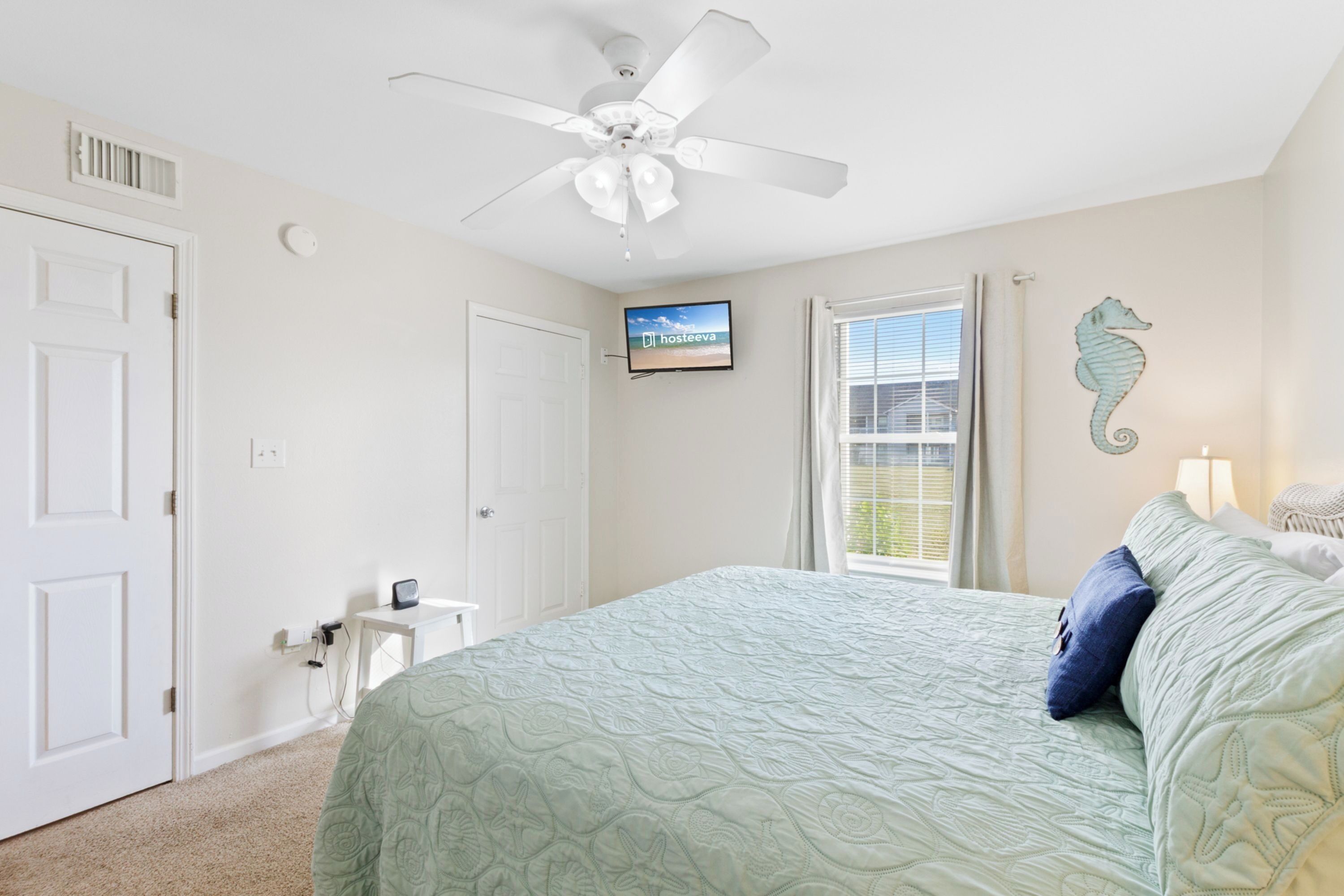 Une chambre à coucher avec un lit, un ventilateur de plafond, une télévision et une fenêtre avec des rideaux.