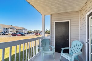 A covered porch with two Adirondack chairs, a view of a parking lot, and a building in the background.