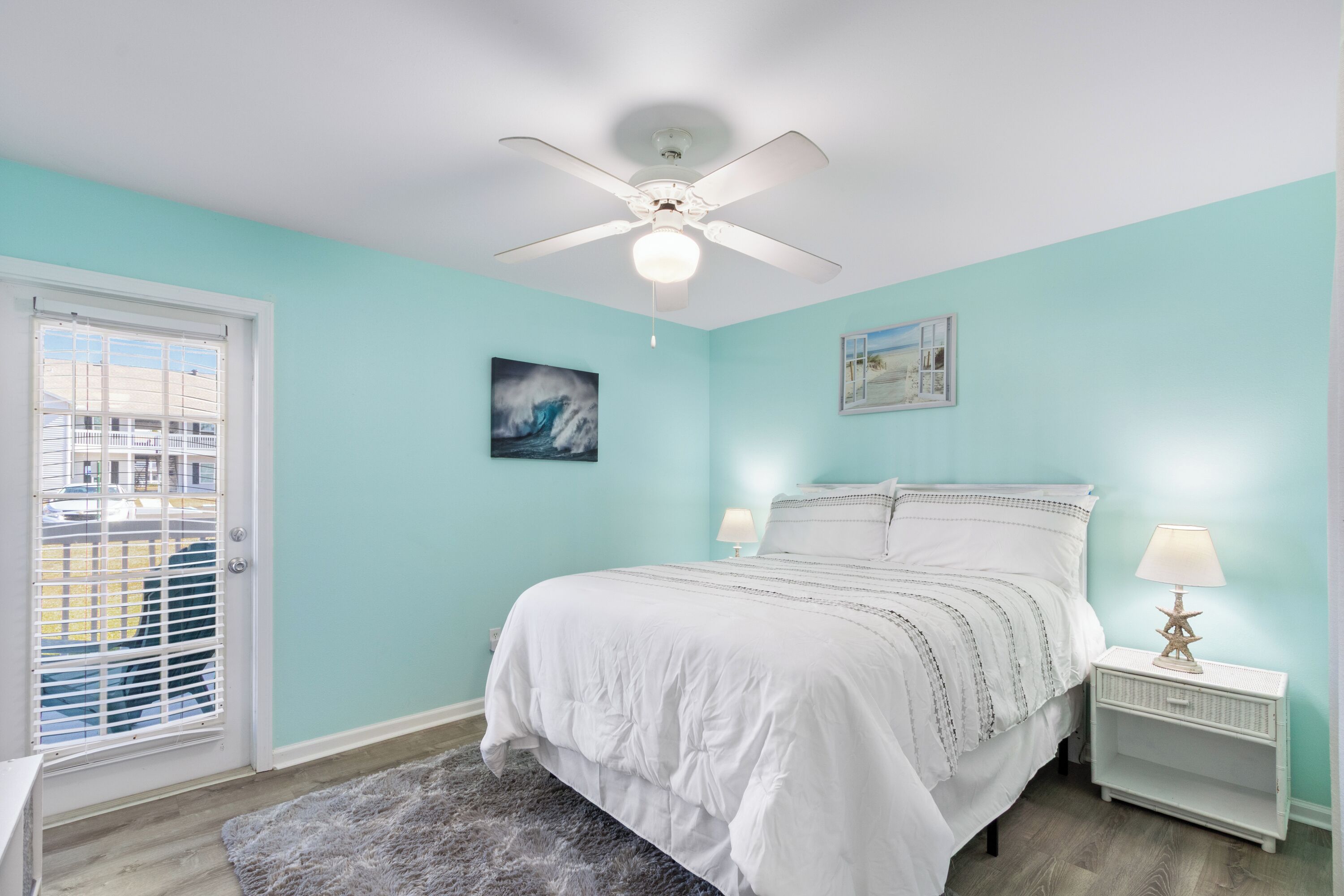 A bedroom with a bed, a ceiling fan, a nightstand with a lamp, and a window with blinds.