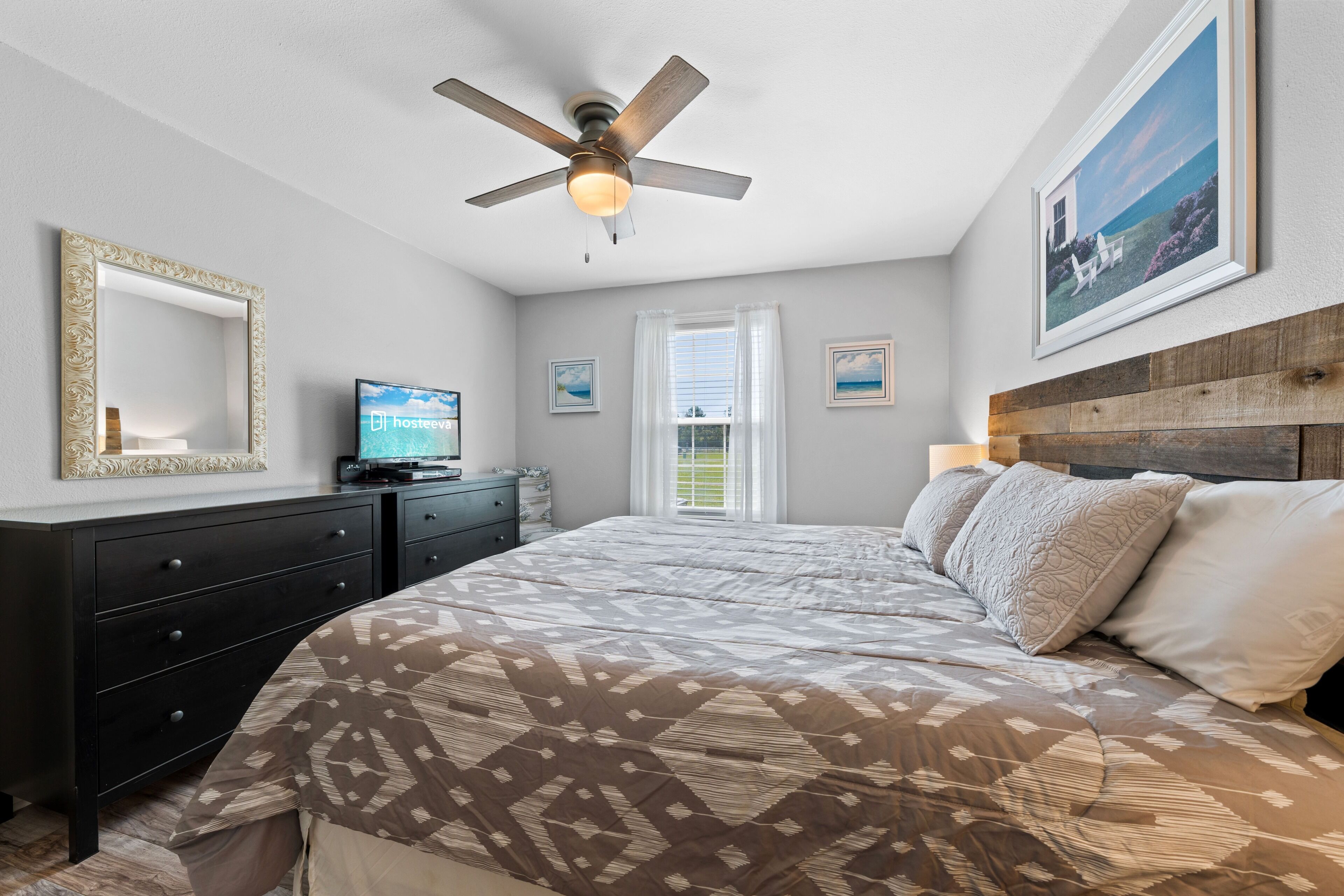 A bedroom with a bed, a ceiling fan, a dresser, a television, and framed pictures on the wall.