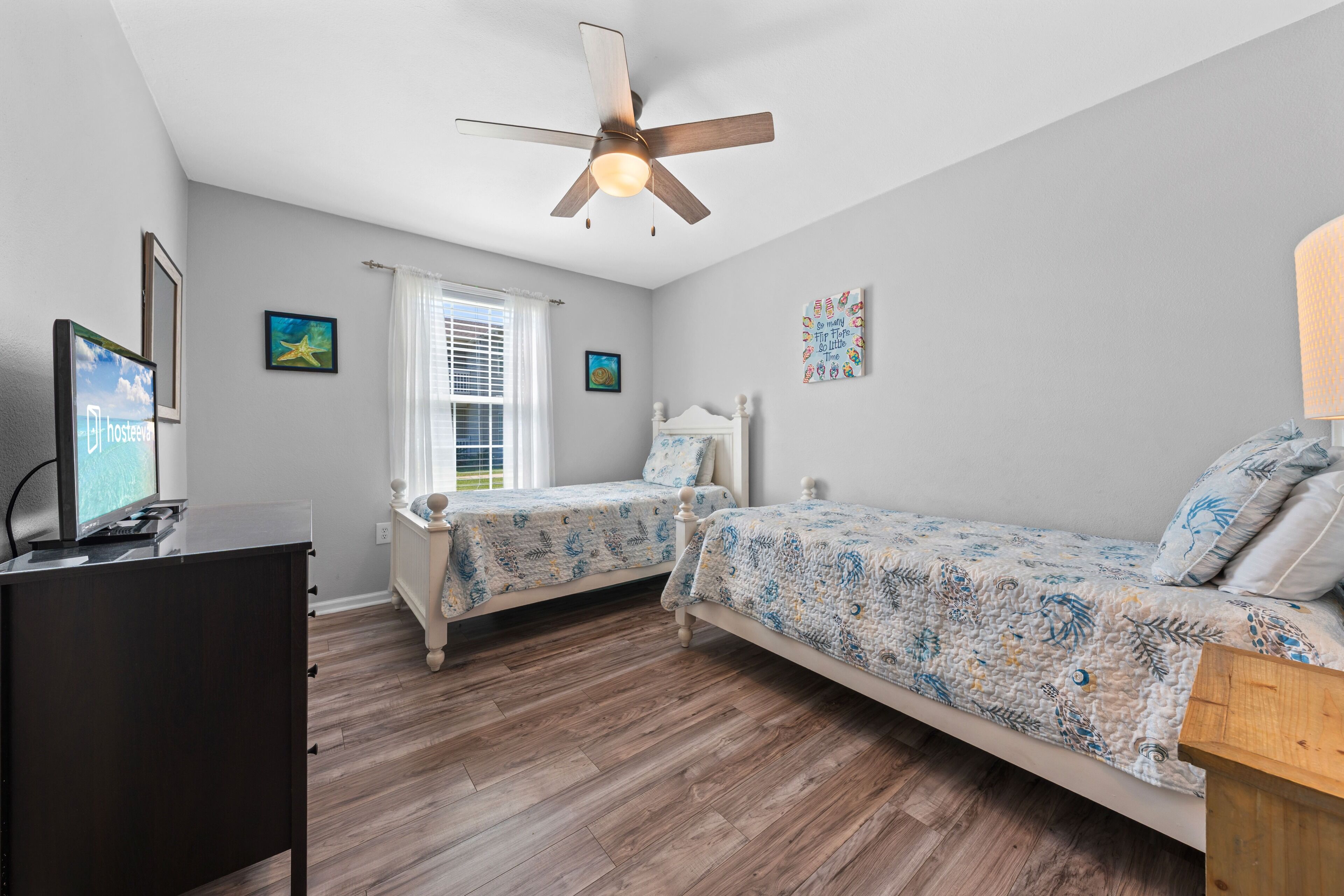 A bedroom with two beds, a ceiling fan, a TV, and a window with blinds.