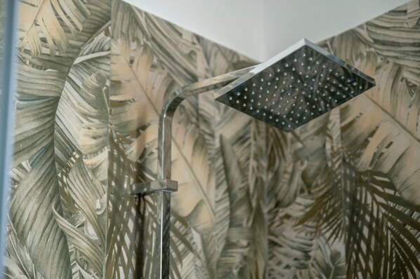 A showerhead with a rain-like spray pattern, mounted on a wall with a tropical leaf pattern.