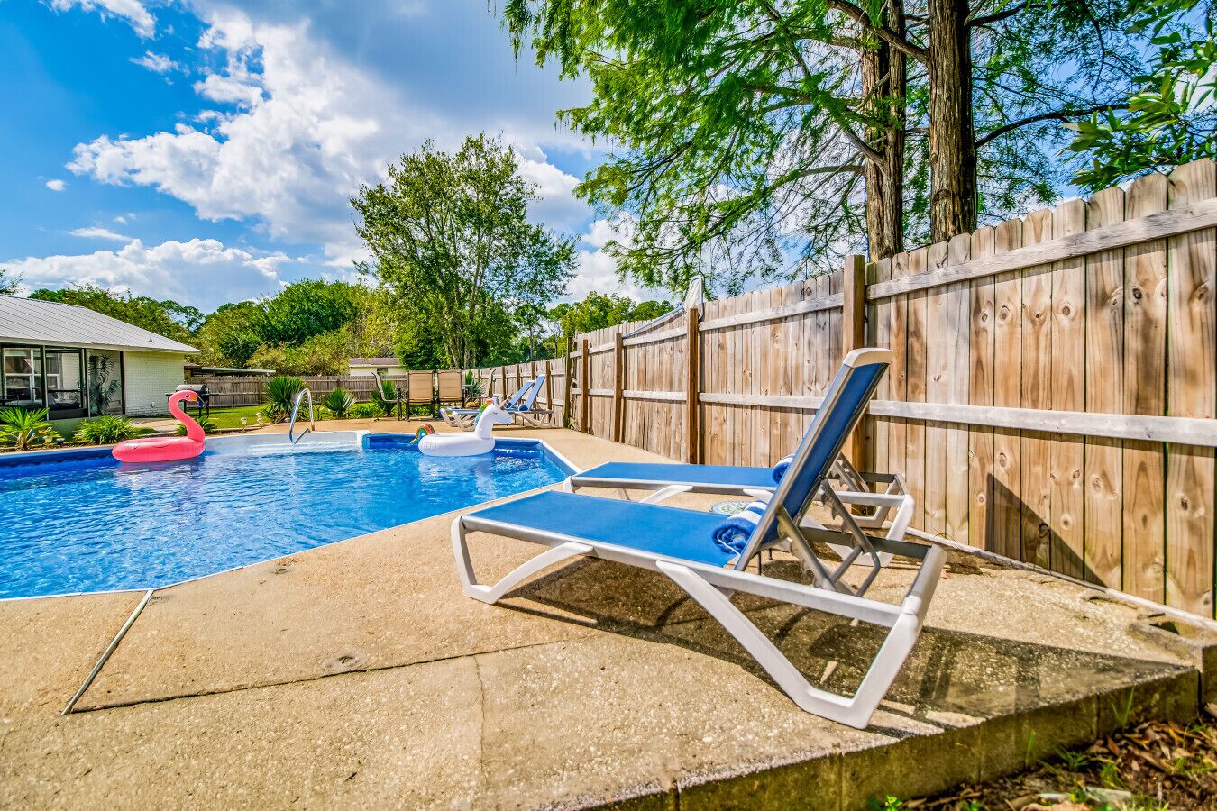 A backyard with a swimming pool, lounge chairs, and a wooden fence.