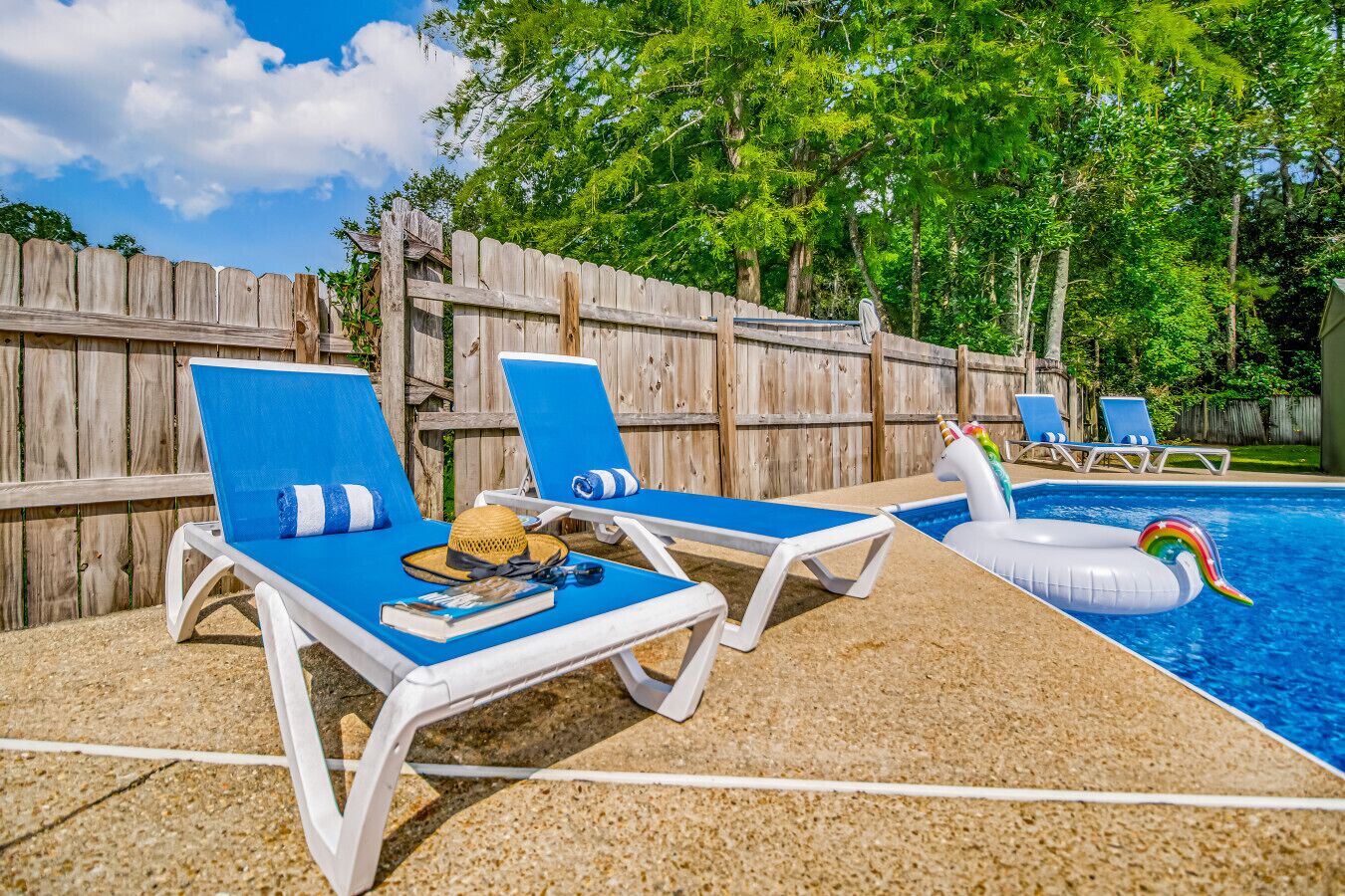 Uma área junto à piscina com espreguiçadeiras, cerca de madeira e um flutuador de unicórnio.