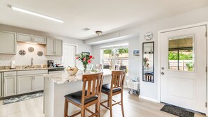 A modern kitchen with white cabinets, a marble countertop, and a dining area with wooden chairs.