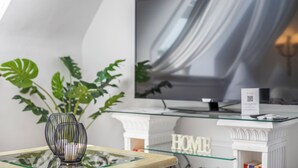 Un salon moderne avec un téléviseur à écran plat fixé sur une table en verre, entouré de grandes plantes vertes.