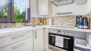 Une cuisine moderne avec un dosseret en pierre, des appareils en acier inoxydable et une fenêtre donnant sur un paysage verdoyant.