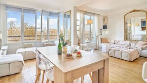 Un ampio soggiorno con tavolo da pranzo in legno, divani bianchi e grandi finestre con vista sulla città.