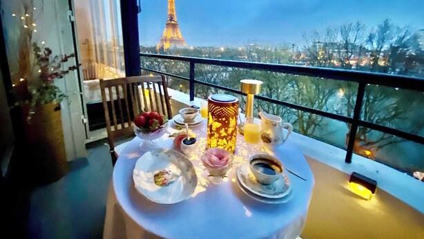 Una tavola apparecchiata per la colazione, con vista sulla Torre Eiffel e un corrimano da balcone.