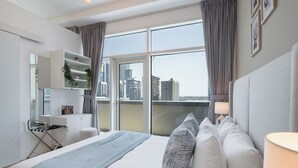 Habitación de hotel moderna con una cama grande, un escritorio, una silla y vistas a la ciudad a través de amplios ventanales.