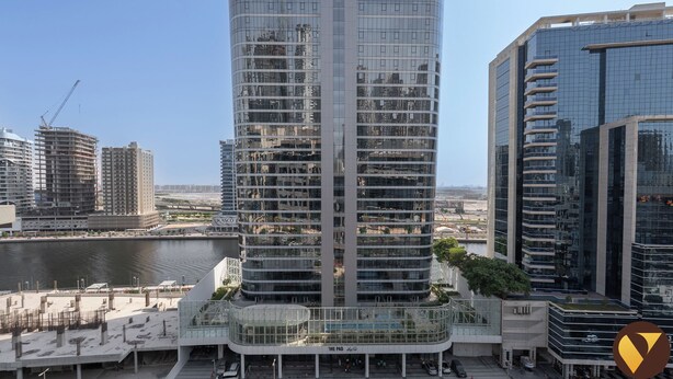 Un edificio de gran altura con varias plantas, fachada de vidrio y un entorno urbano circundante con otros edificios y una masa de agua.