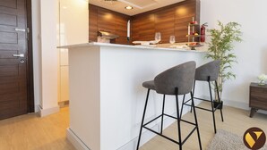 Una cocina moderna con una isla central, dos taburetes de bar y una mesita auxiliar con una planta.