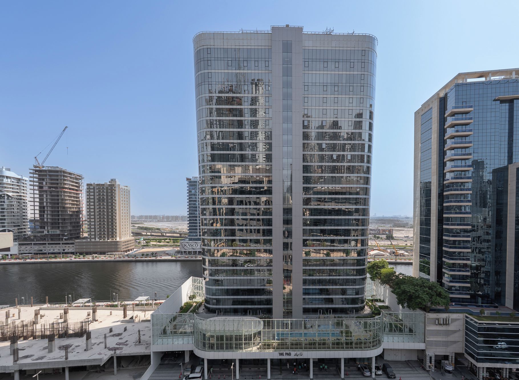 A high-rise building with multiple floors, a glass facade, and a surrounding urban environment with other buildings and a body of water.