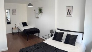 Una habitación de hotel moderna con una cama grande, una cama más pequeña, una mesita de noche, una lámpara y un espejo.