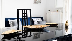 A dining table with decorative plates, a pineapple, and a chair in a modern room with a blue sofa and a radiator.