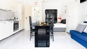 A modern kitchen with white cabinets, a black dining table, and a blue sofa in the living area.
