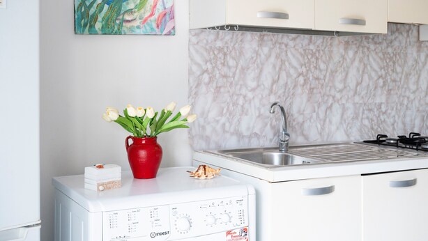 Une cuisine avec un dosseret en marbre, un évier, une cuisinière et un vase rouge orné de fleurs, posé sur un appareil électroménager blanc.